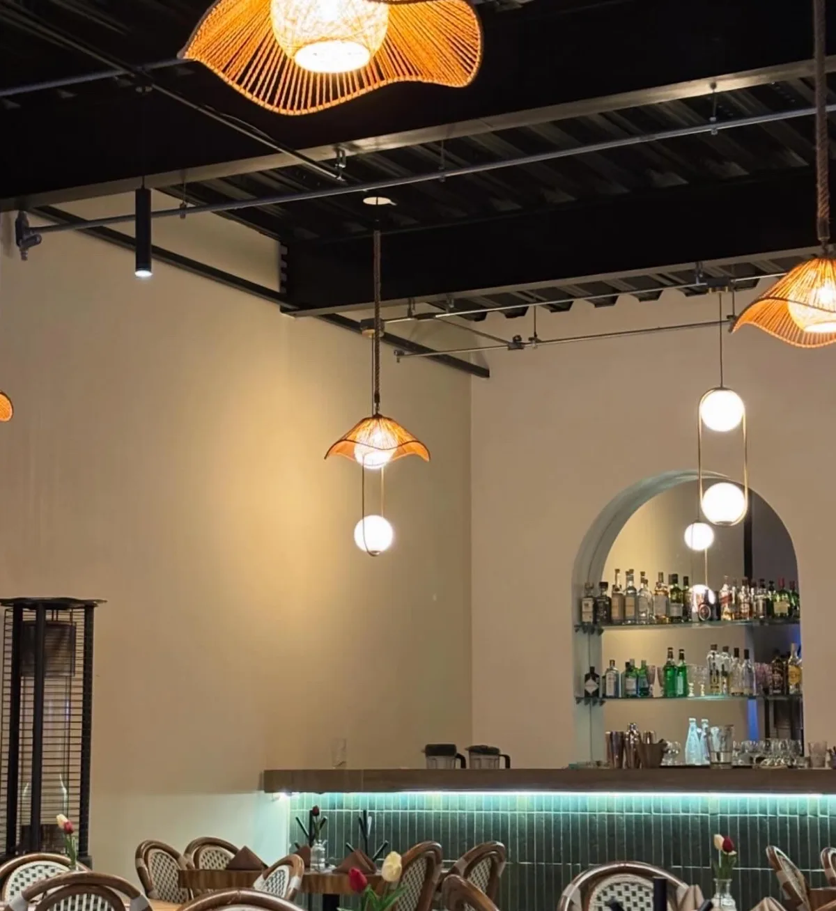 La barra de Querena bajo su arco: el frente de azulejo verde, los estantes iluminados con botellas y las lámparas de fibra colgando.