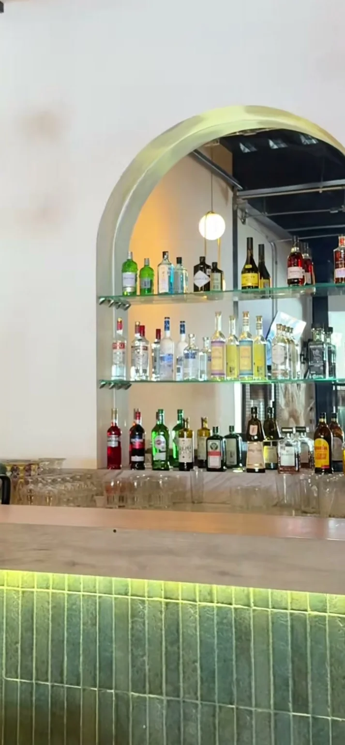 La barra de Querena: el arco de obra, los estantes iluminados con las botellas y el azulejo verde del frente.