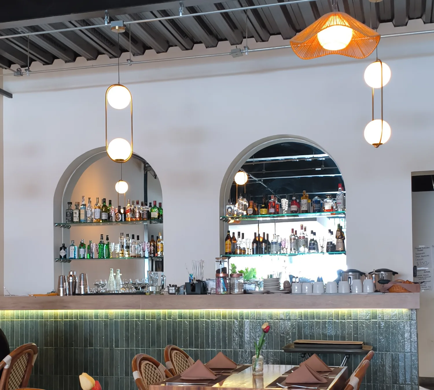 La barra de Querena: los dos arcos con las botellas retroiluminadas, el frente de azulejo verde y las lámparas de fibra colgando.