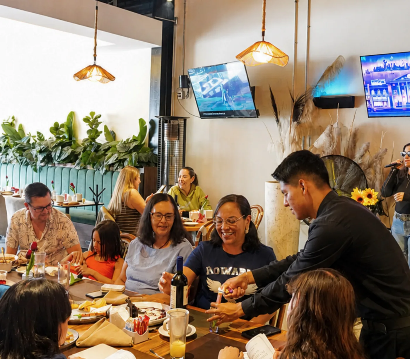 Una celebración en el salón de Querena: una mesa larga con la familia sentada y un mesero sirviendo.