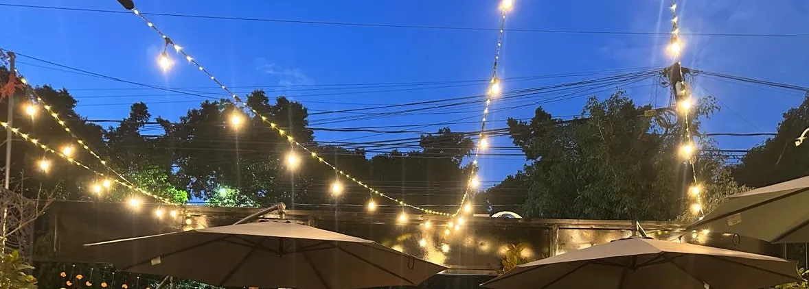 La terraza de Querena al caer la tarde: focos de cuerda encendidos entre las sombrillas, las sillas de bejuco puestas y el cielo todavía azul.