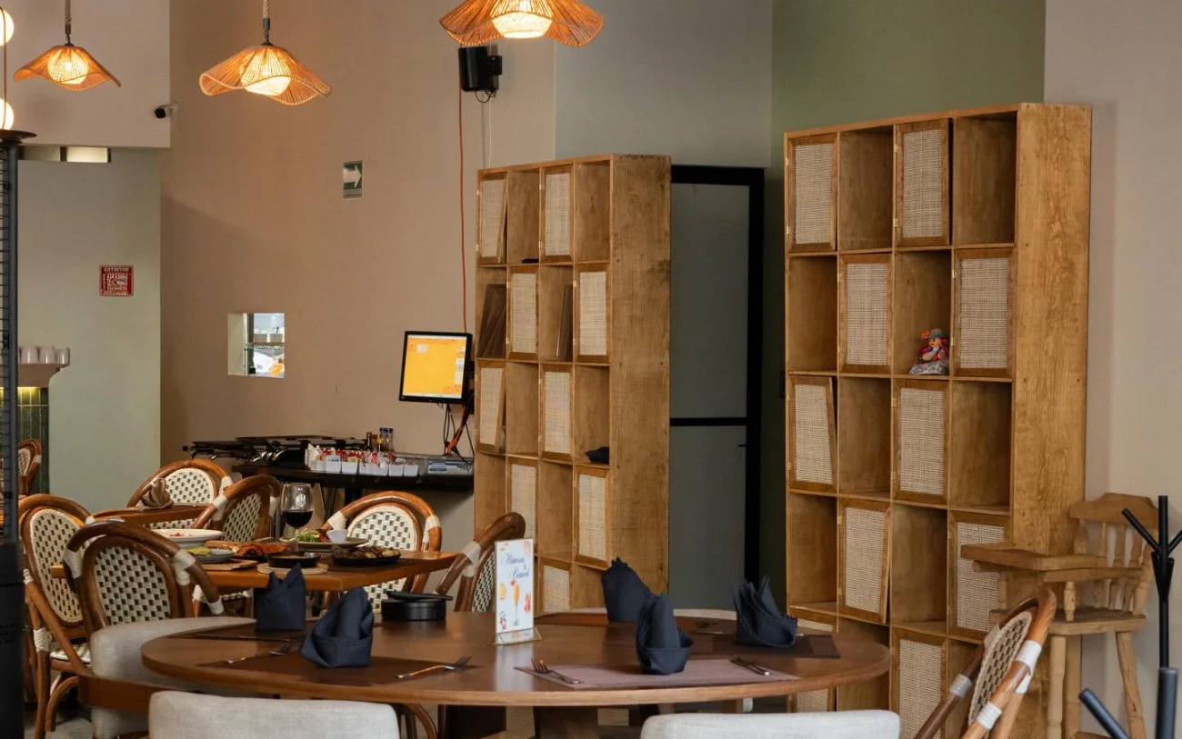 El salón de Querena: libreros de madera y bejuco, una mesa redonda puesta y sillas de bejuco.