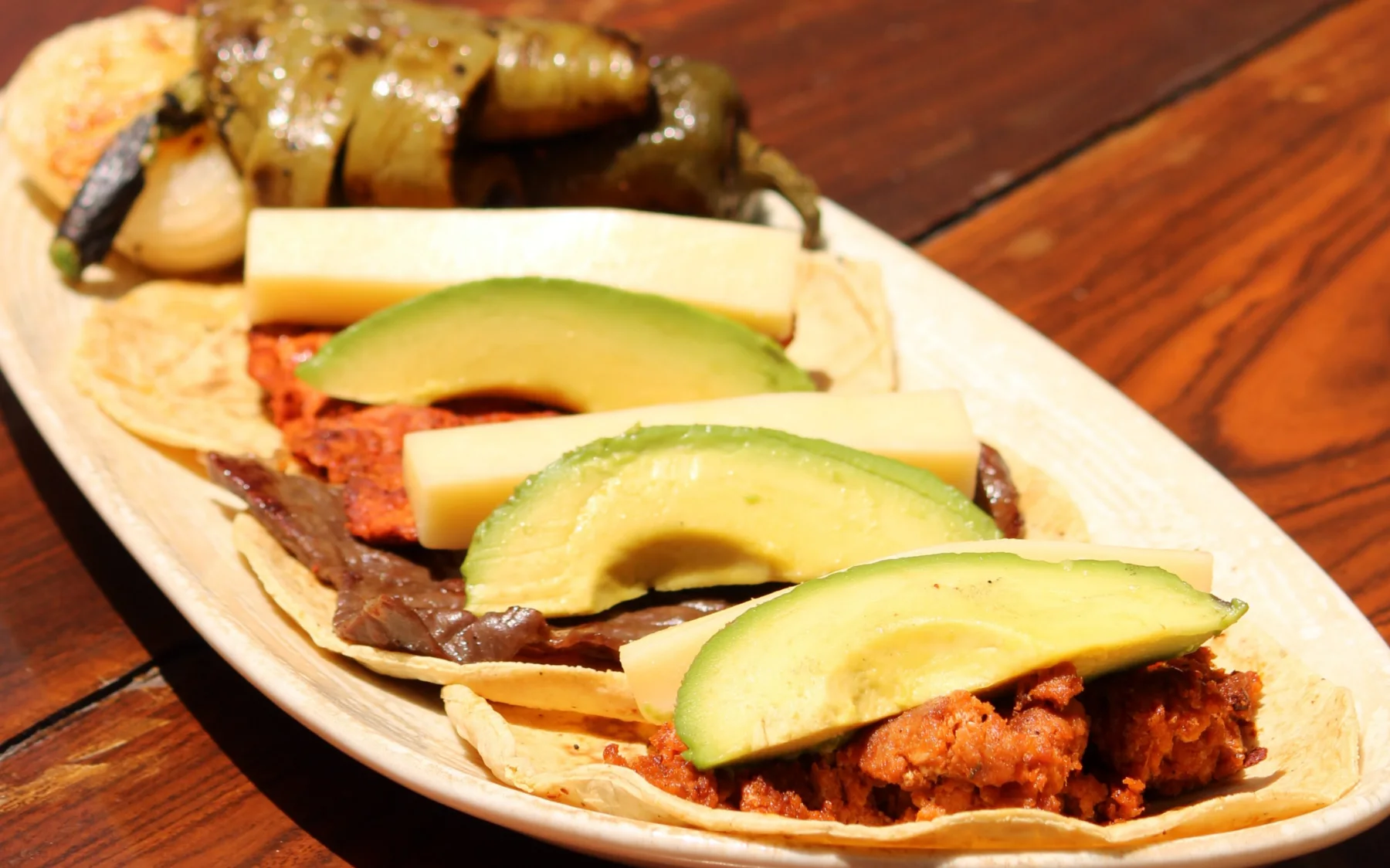 Tacos de cecina de Yecapixtla con nopales asados, aguacate y queso, sobre una mesa de madera.