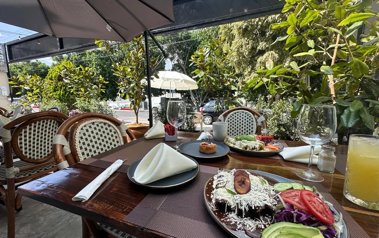 Un desayuno en la terraza de Querena: platos servidos, copas y jugo sobre una mesa de madera, con las sillas de bejuco y las plantas alrededor.