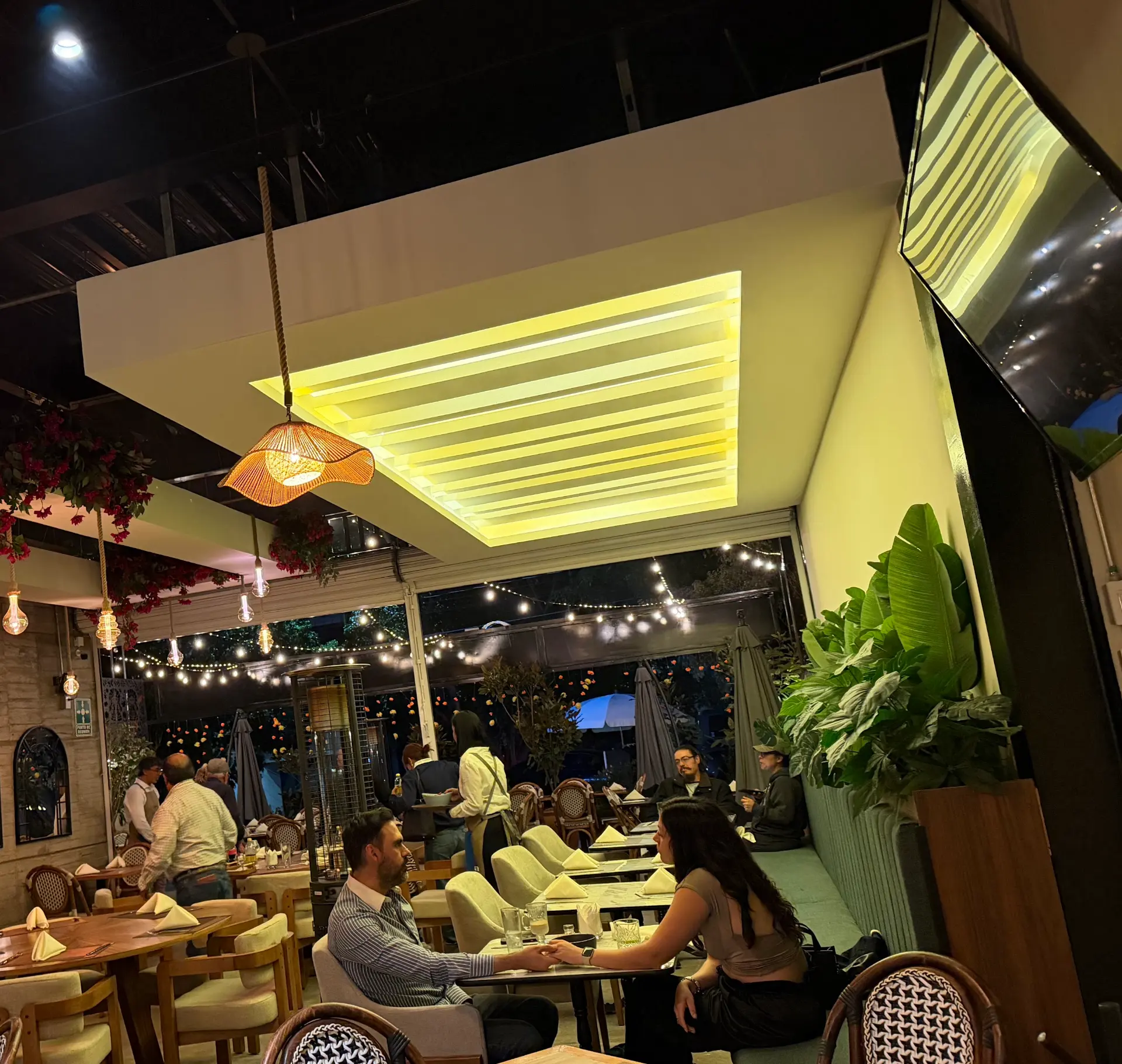 El salón cubierto de Querena al anochecer, con los focos de cuerda encendidos y la bugambilia del techo.