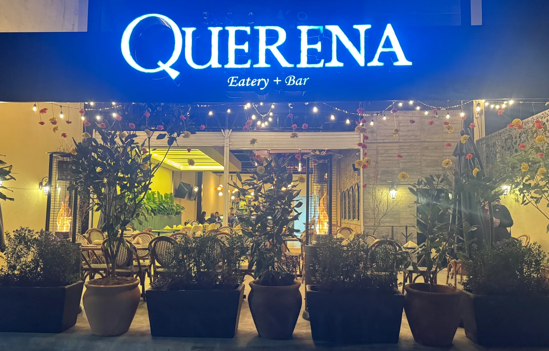 La fachada de Querena al anochecer con el letrero encendido y la terraza iluminada.