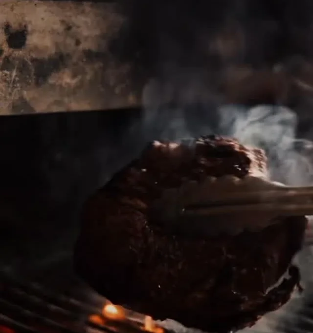 Un corte de carne sobre la parrilla, con las brasas encendidas debajo y el humo subiendo.
