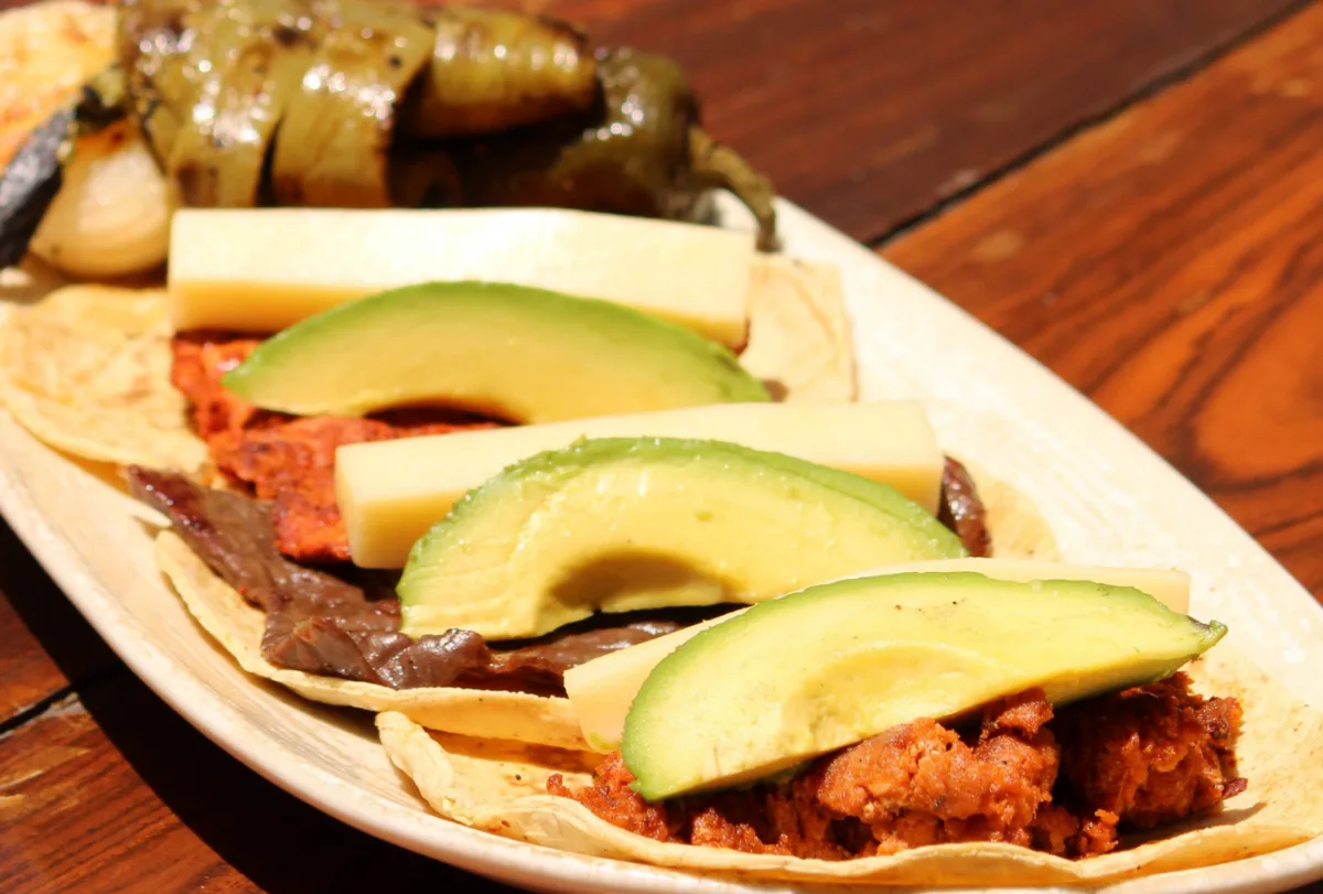 Tacos de cecina de Yecapixtla con nopal asado, láminas de aguacate y queso, en un plato ovalado.