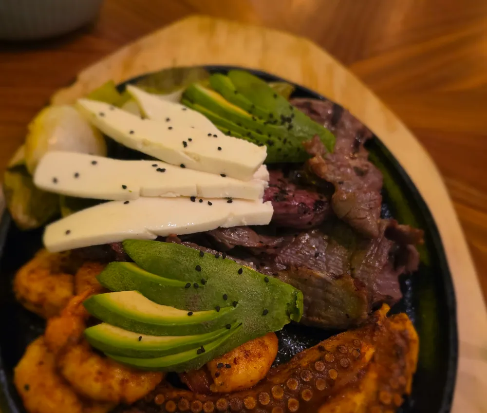 Comal negro con carne, tentáculos de pulpo, tiras de queso blanco, aguacate y plátano frito.