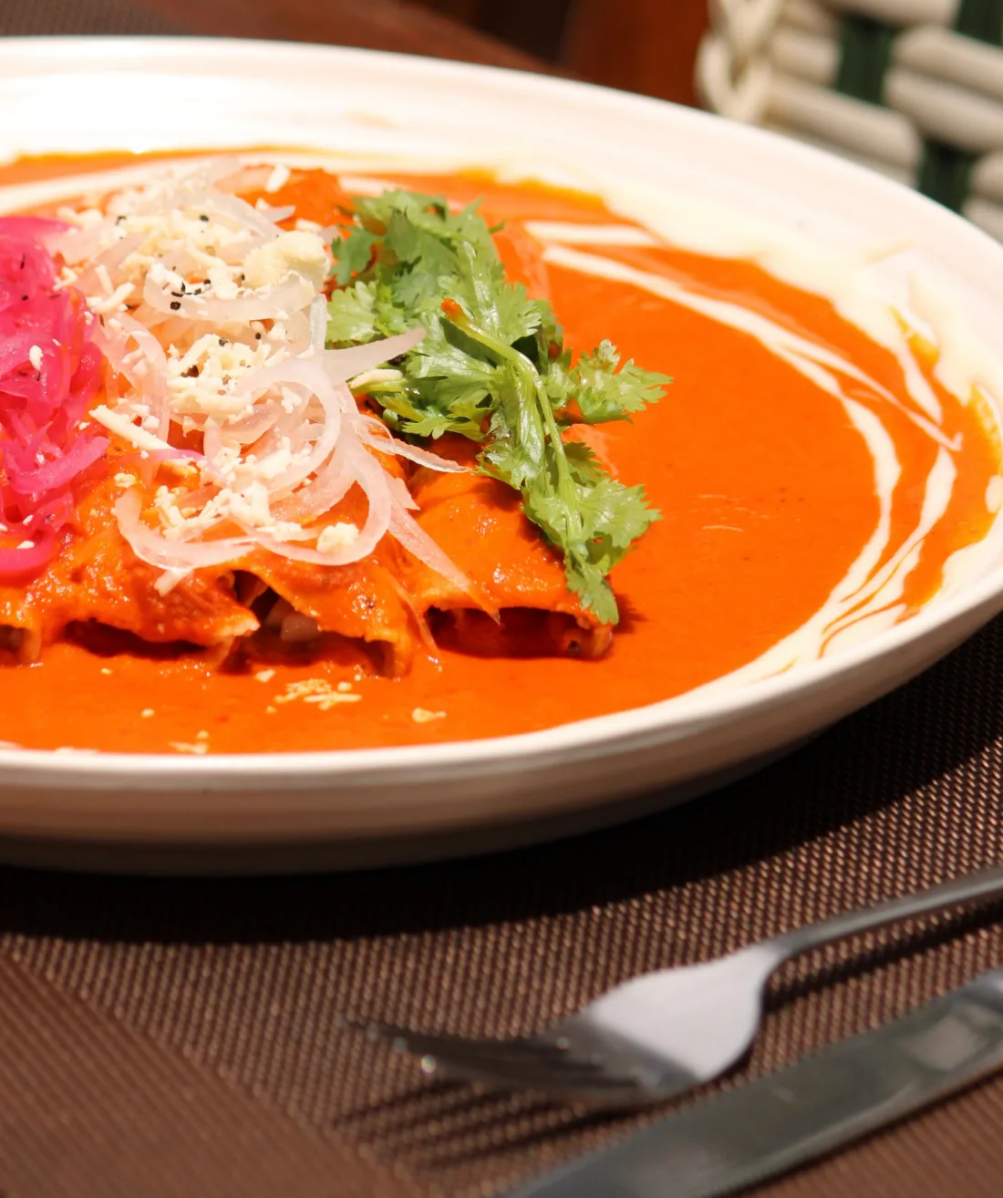 Enchiladas bañadas en salsa roja, con cebolla morada encurtida, queso rallado y cilantro, en un plato blanco.