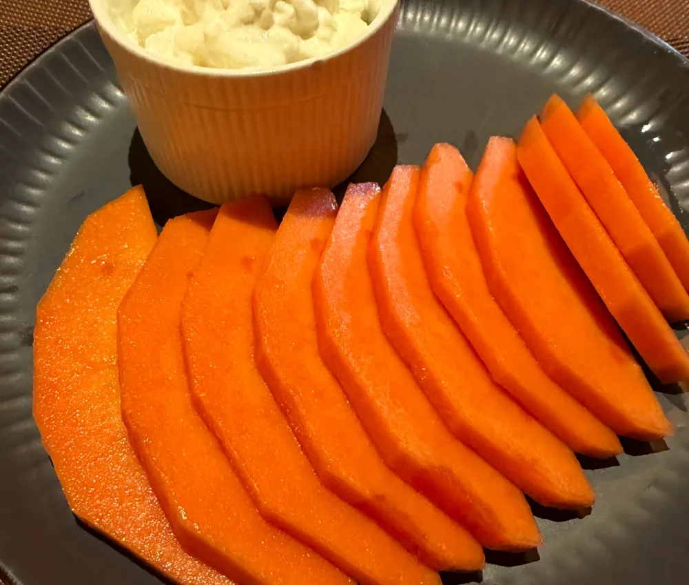 Abanico de rebanadas de papaya sobre un plato oscuro, con un cuenco de yogur al lado.