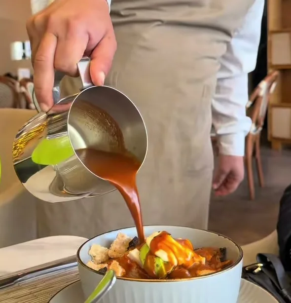 Un mesero de Querena sirviendo salsa caliente sobre un plato, delante del comensal.